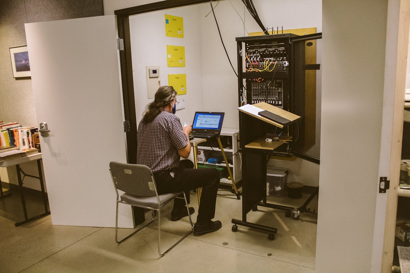 Person in a plaid shirt types on a laptop near server racks.